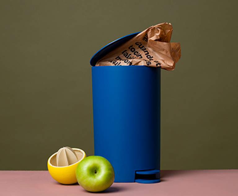 Composition of a lemon squeezer, an apple and a trashbin with a paper package sticking out of it